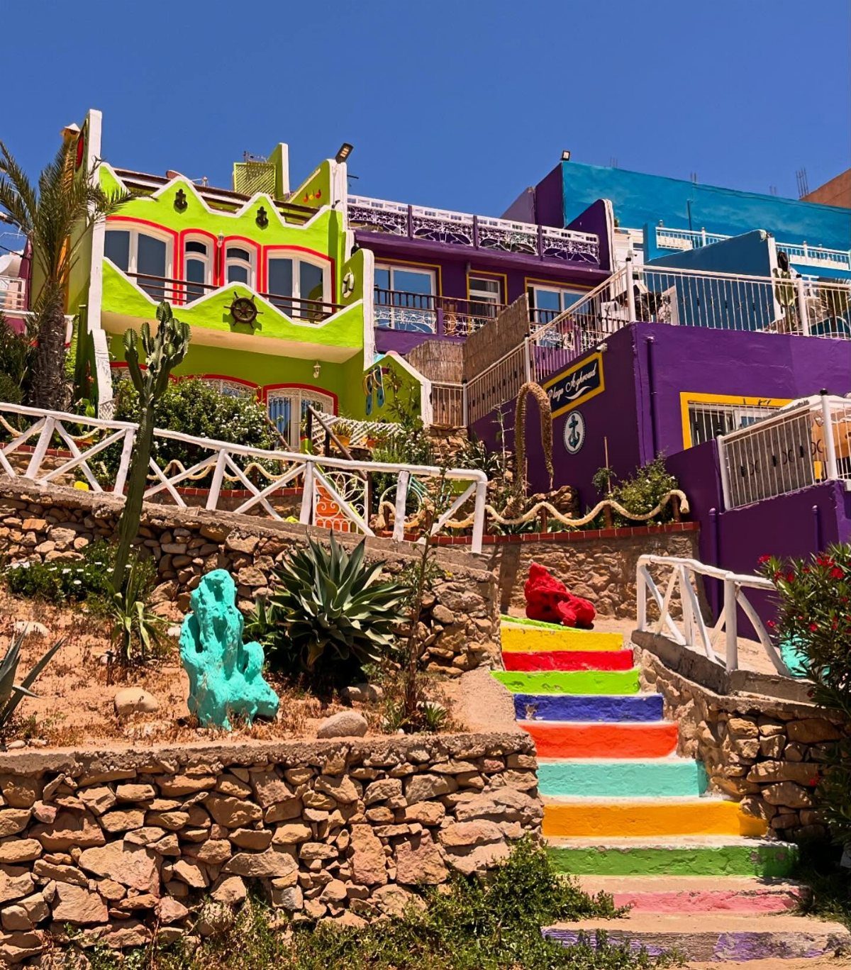 16 Cheap Pretty Places to Travel on a Tight Budget 15 Colorful houses and a rainbow staircase on a sunny hillside with stone walls.