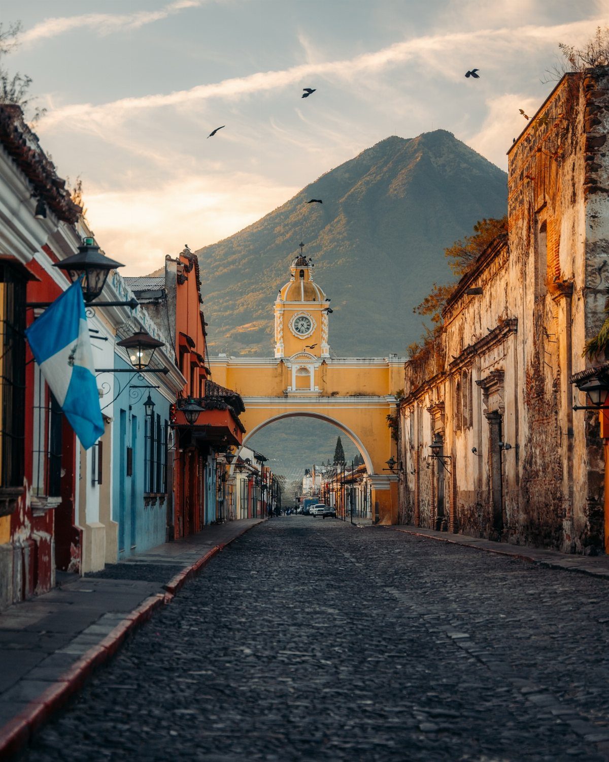 16 Cheap Pretty Places to Travel on a Tight Budget 6 Cobblestone street with colorful buildings and a yellow arch before a large mountain.