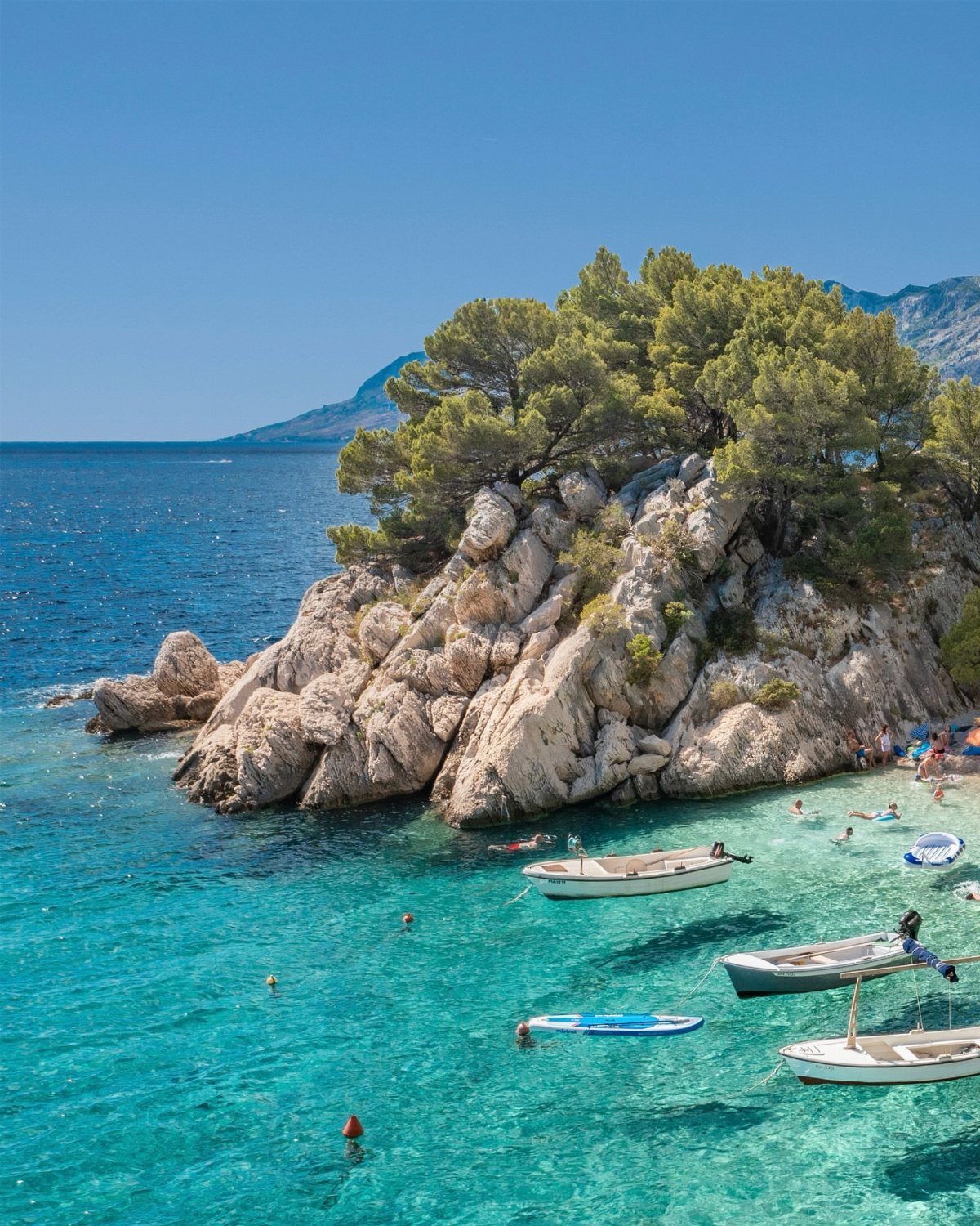 16 Cheap Pretty Places to Travel on a Tight Budget 12 Turquoise coastal waters with white rocky cliffs, pine trees, and small white boats.