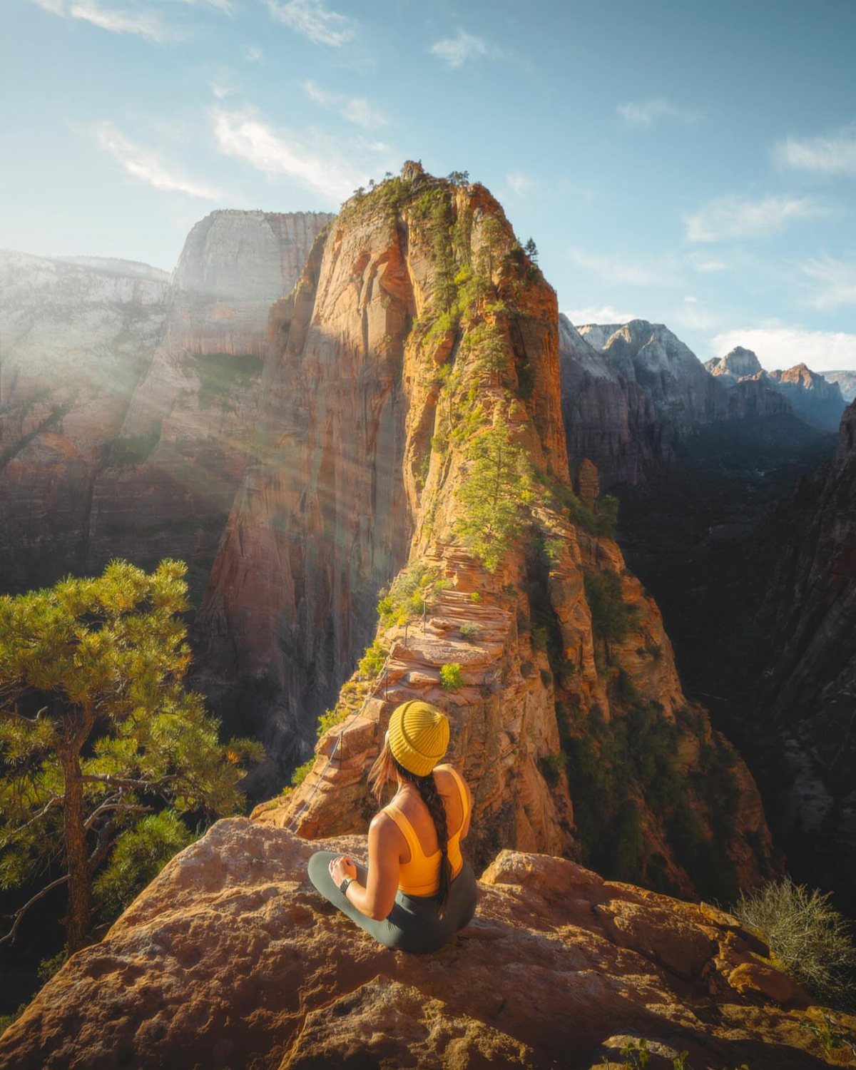 16 Cheap Pretty Places to Travel on a Tight Budget 3 Woman sitting on a rocky ledge overlooking steep red sandstone cliffs in Zion Canyon.