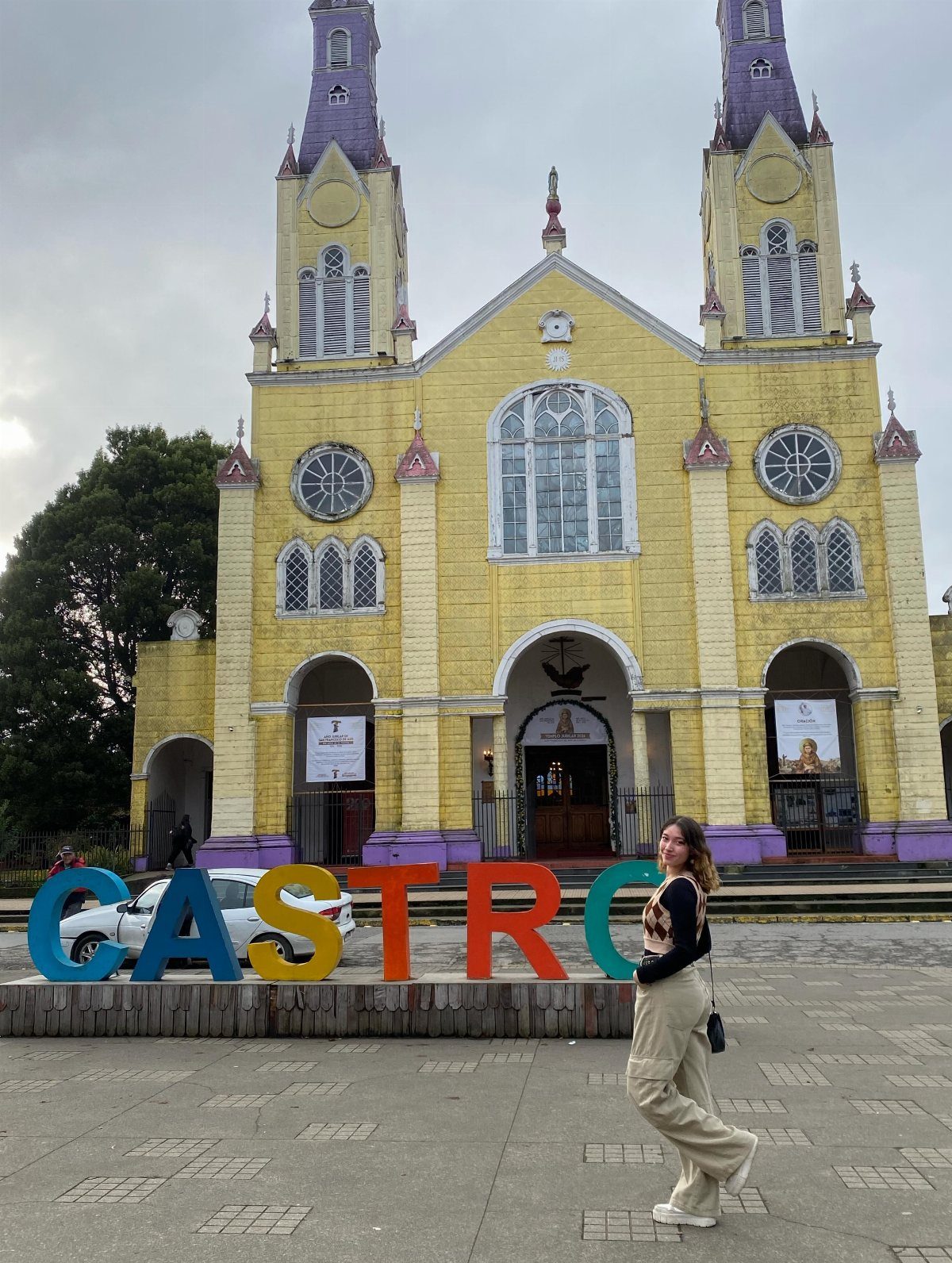 Woman posing by colorful CASTRO sign in front of a yellow church in Chile