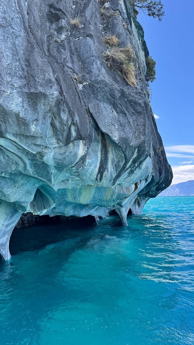 Marble cliff with swirling blue patterns and caves over turquoise water