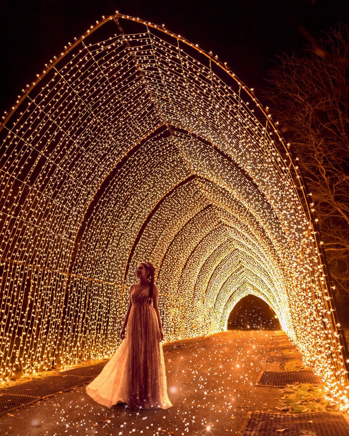 14 Christmas Places to Visit for Holiday Lights and Markets 5 Woman in a gown standing inside a glowing tunnel of golden Christmas lights