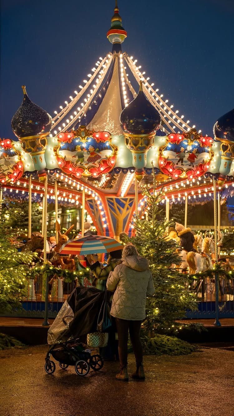 14 Christmas Places to Visit for Holiday Lights and Markets 14 Illuminated carousel at a Christmas market with a person and baby stroller.