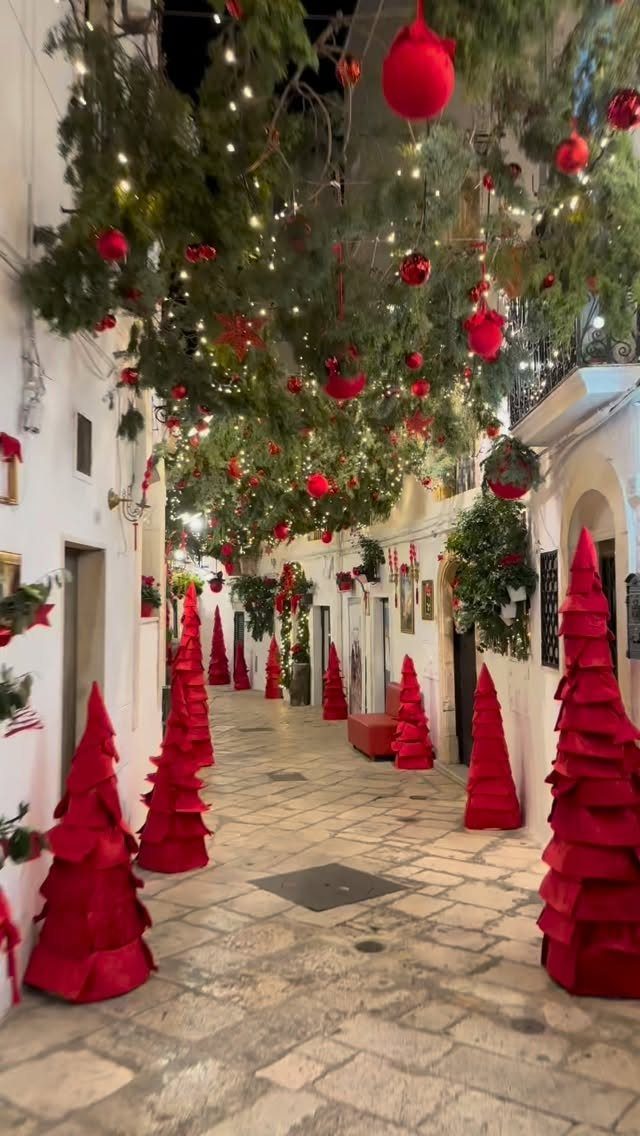 14 Christmas Places to Visit for Holiday Lights and Markets 10 Cobblestone alleyway decorated with red conical trees and overhead Christmas garlands and lights.