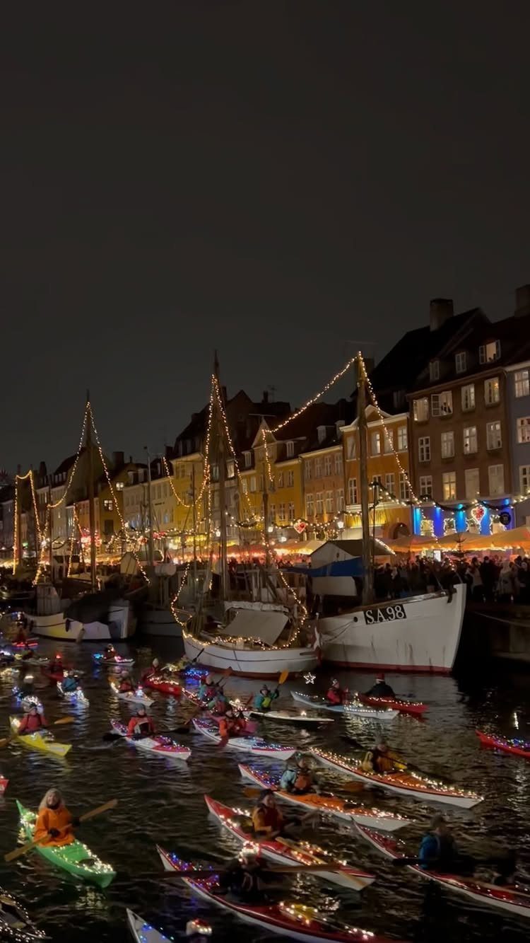 14 Christmas Places to Visit for Holiday Lights and Markets 8 Illuminated harbor with decorated buildings and kayakers in light-up boats at night.