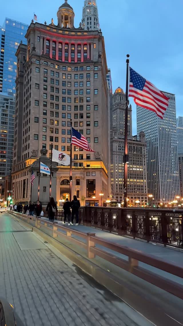 12 Cities to Visit in the U.S. and Abroad for 2026 9 Tall skyscrapers and American flags along a city bridge at twilight.