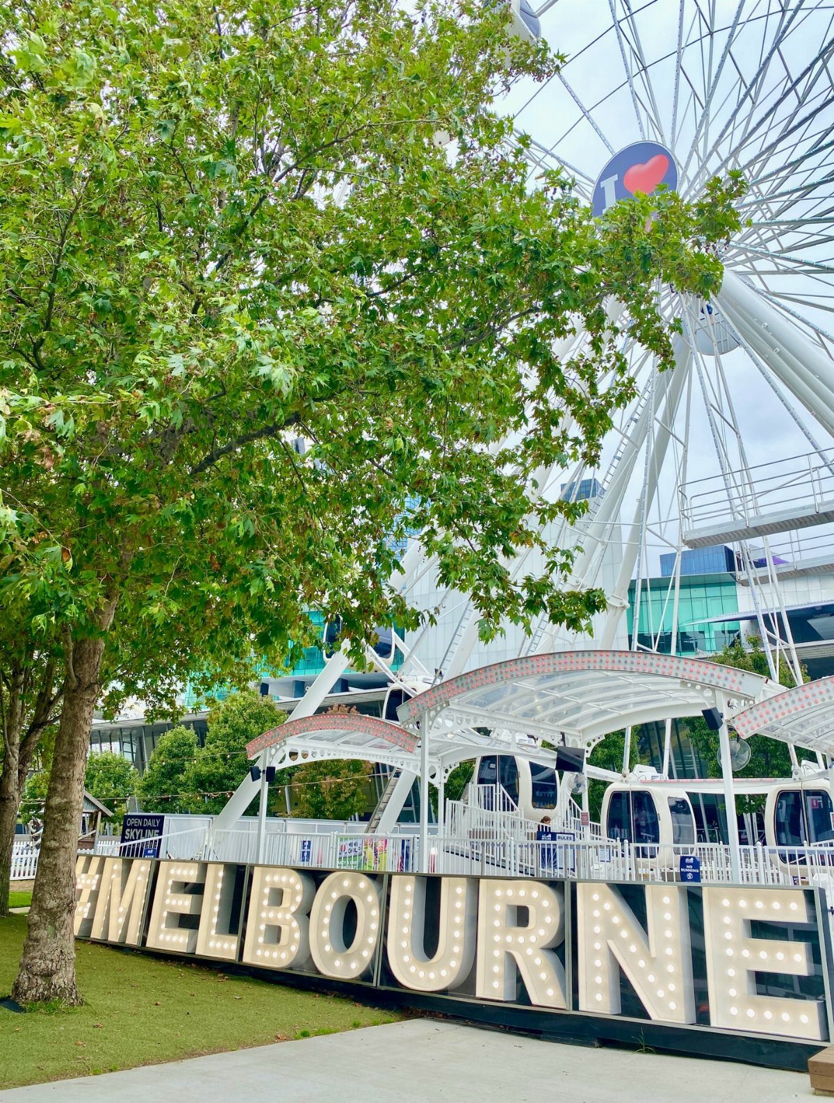 12 Cities to Visit in the U.S. and Abroad for 2026 8 Large illuminated Melbourne sign in front of a white Ferris wheel and green trees.