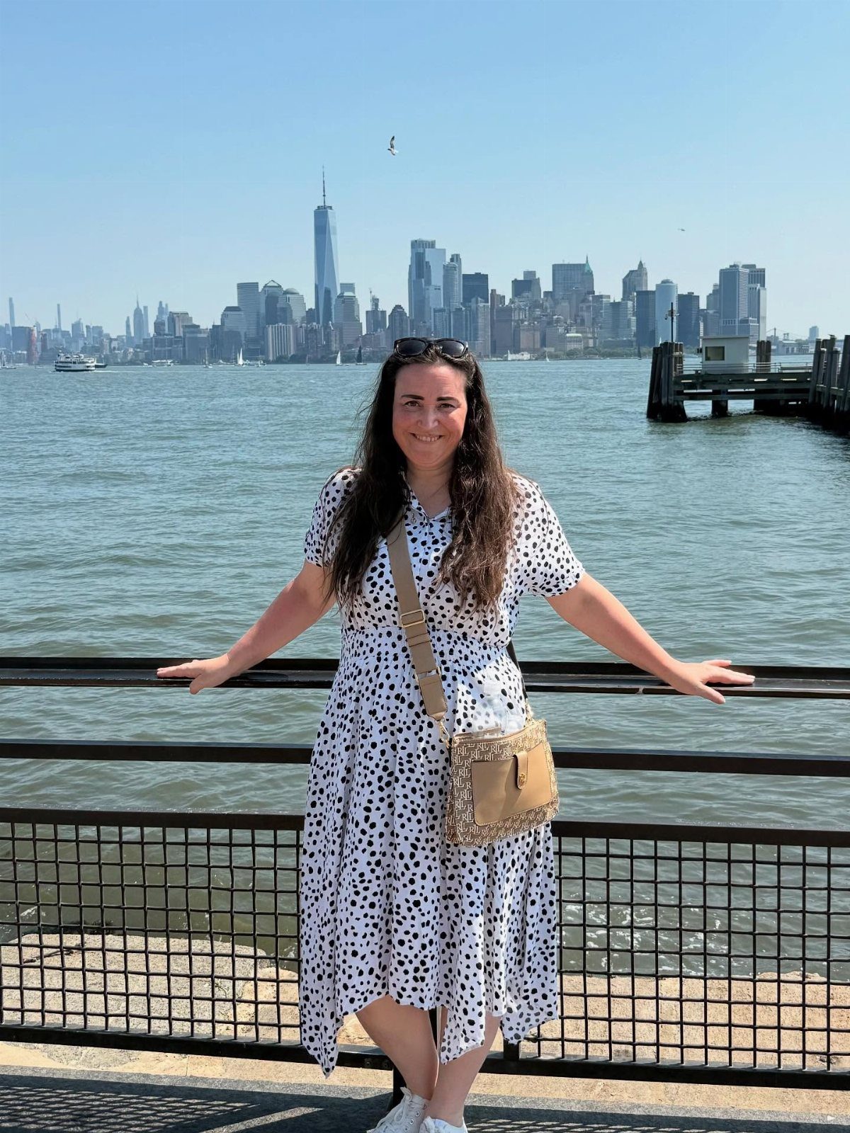 12 Cities to Visit in the U.S. and Abroad for 2026 1 Woman in polka dot dress posing before the New York City skyline and waterfront.