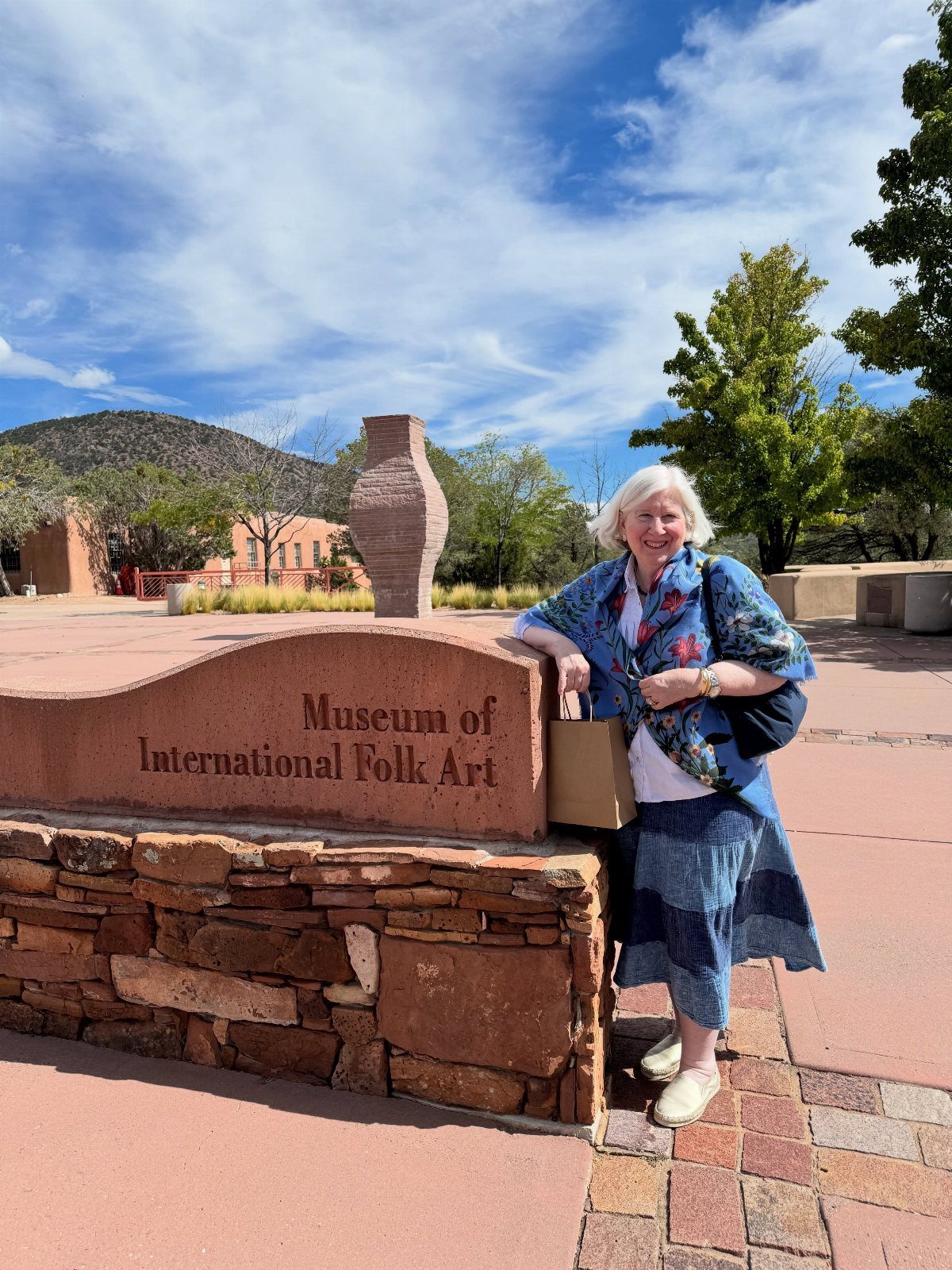 12 Cities to Visit in the U.S. and Abroad for 2026 5 Woman standing by the Museum of International Folk Art sign in Santa Fe