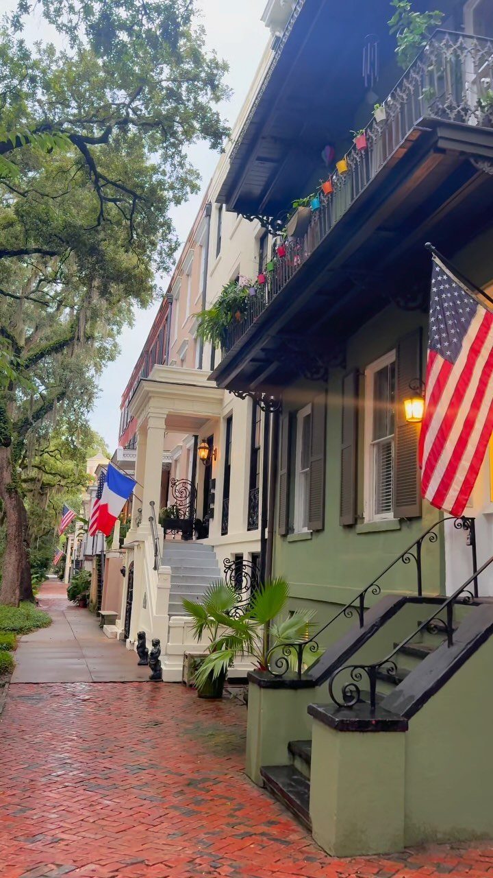 12 Cities to Visit in the U.S. and Abroad for 2026 6 Historic houses with balconies and an American flag along a red brick sidewalk.