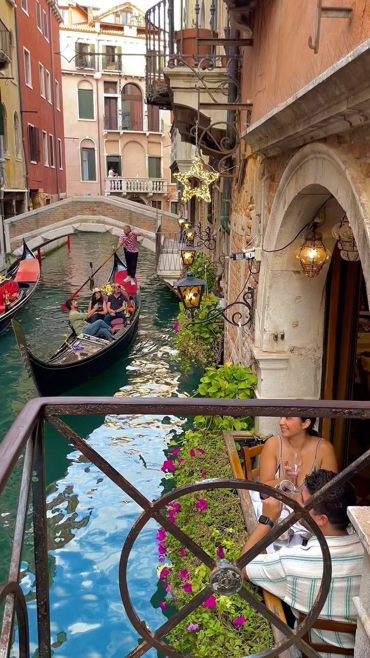 12 Cities to Visit in the U.S. and Abroad for 2026 11 Venice canal with a gondola, colorful buildings, and people dining on a balcony.