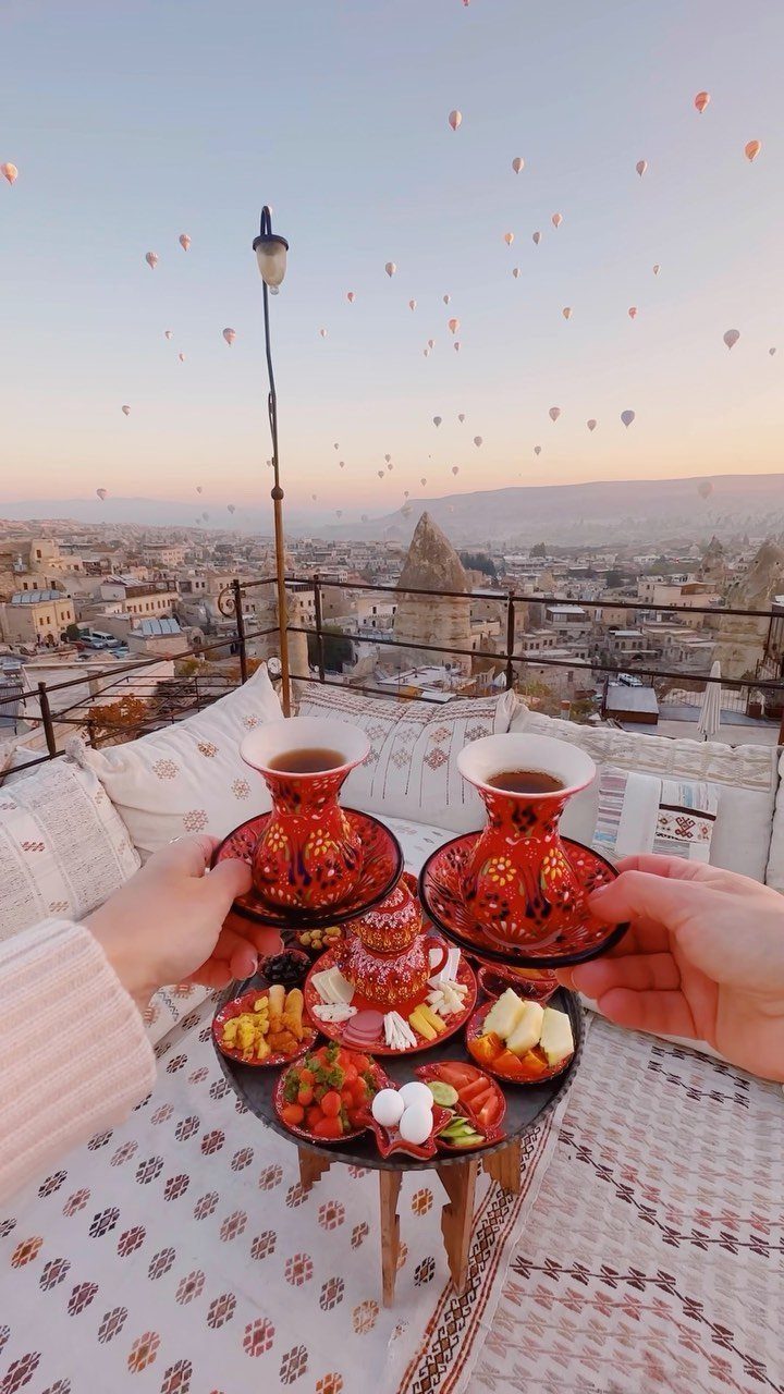 Breakfast on a rooftop terrace with hot air balloons floating over Cappadocia valley.