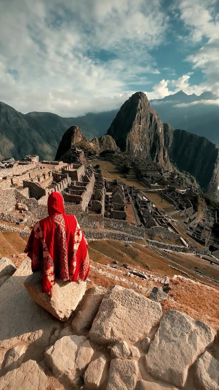 Person in red poncho overlooking the ancient stone ruins of Machu Picchu and mountains.