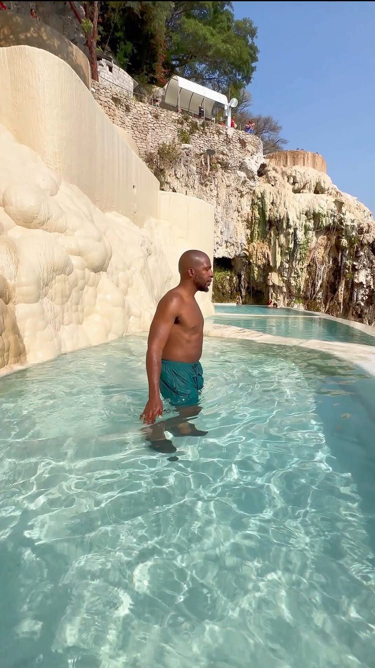 Man standing in a turquoise pool surrounded by pale limestone rock formations.