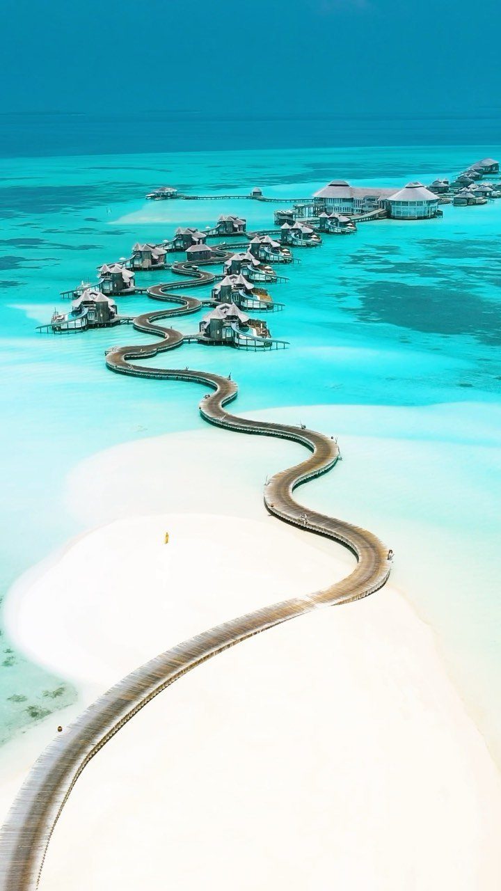 Winding wooden boardwalk leading to thatched-roof overwater bungalows in turquoise tropical waters.