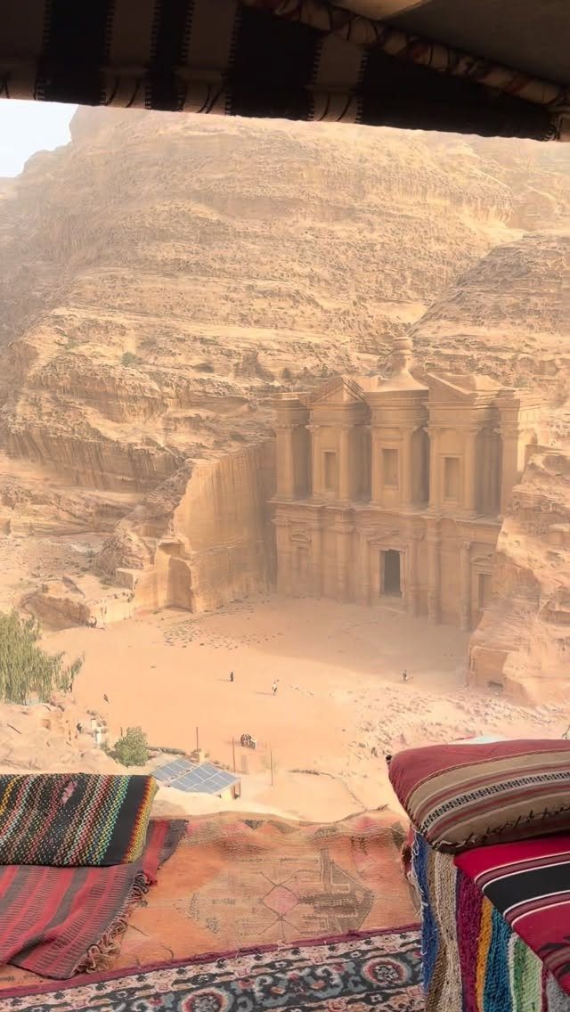 The Treasury at Petra carved into sandstone cliffs viewed from a rug-covered terrace.