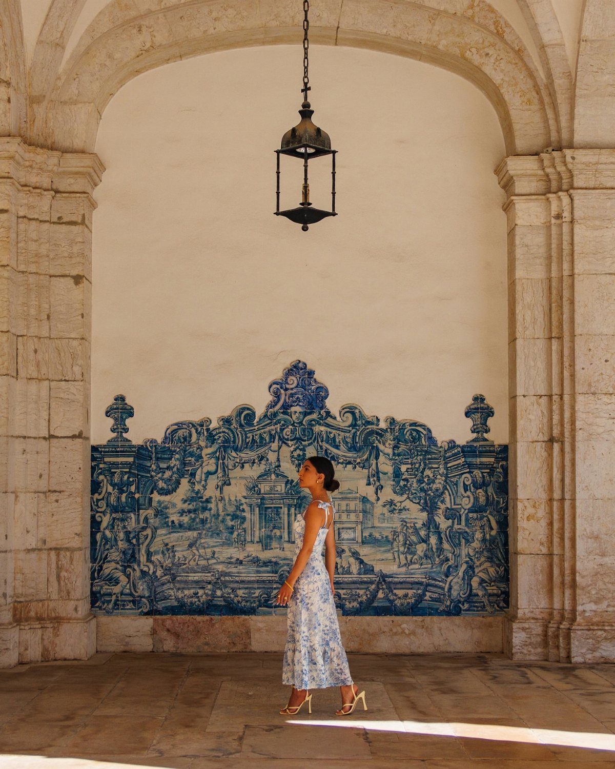 Woman in floral dress standing before a blue and white Portuguese tile mural.