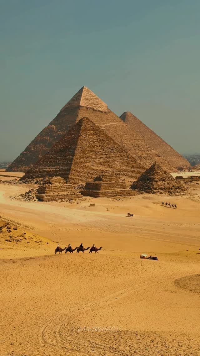 Three ancient Egyptian pyramids in a sandy desert with people riding camels.