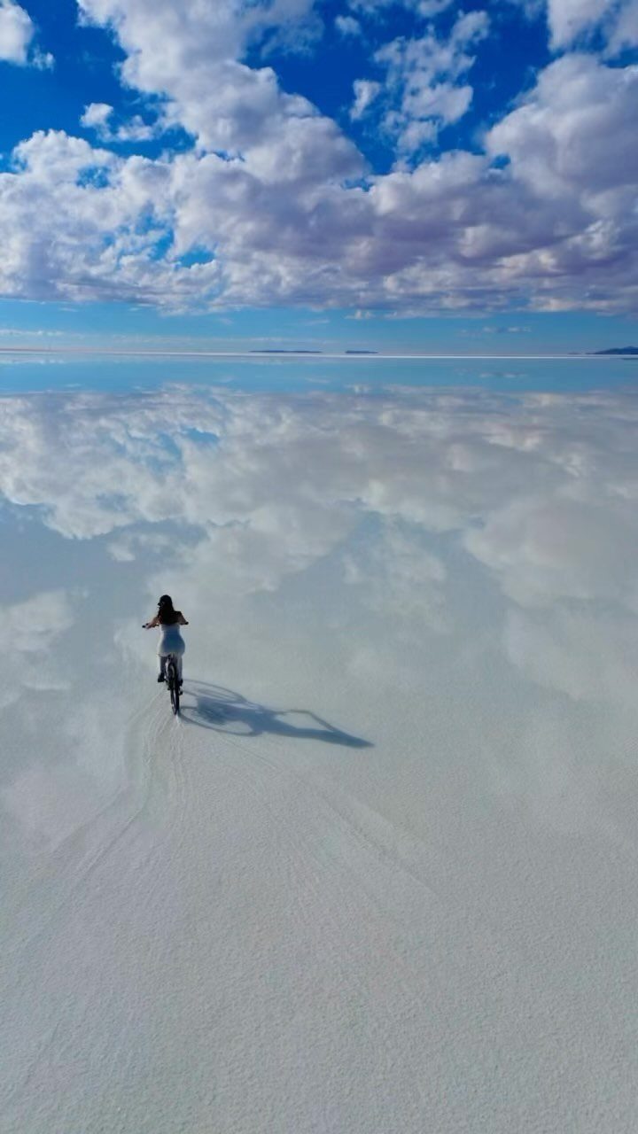 Person riding a bicycle across the reflective white surface of Salar de Uyuni.
