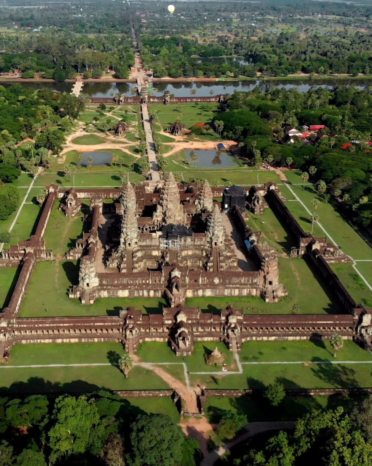 Angkor Wat temple complex with stone towers and green lawns seen from above.