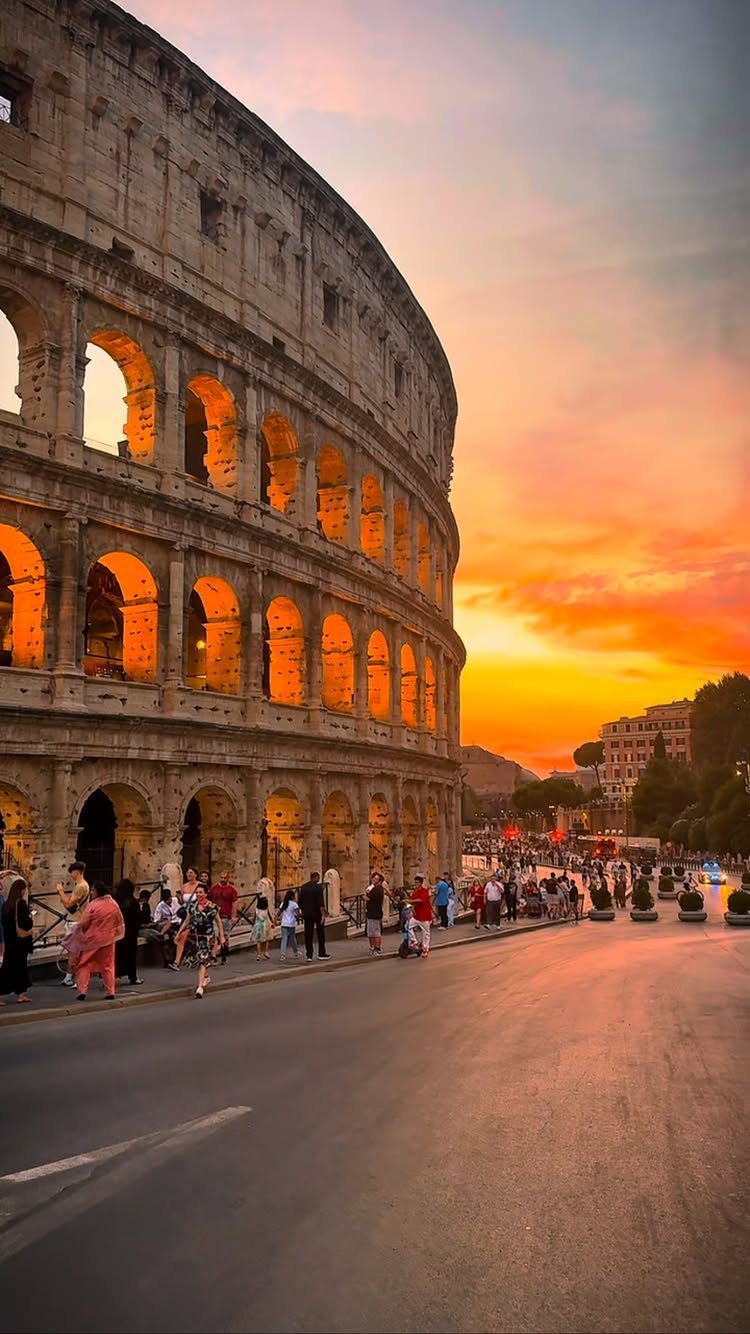 The Colosseum amphitheater illuminated at sunset with people walking along the street.