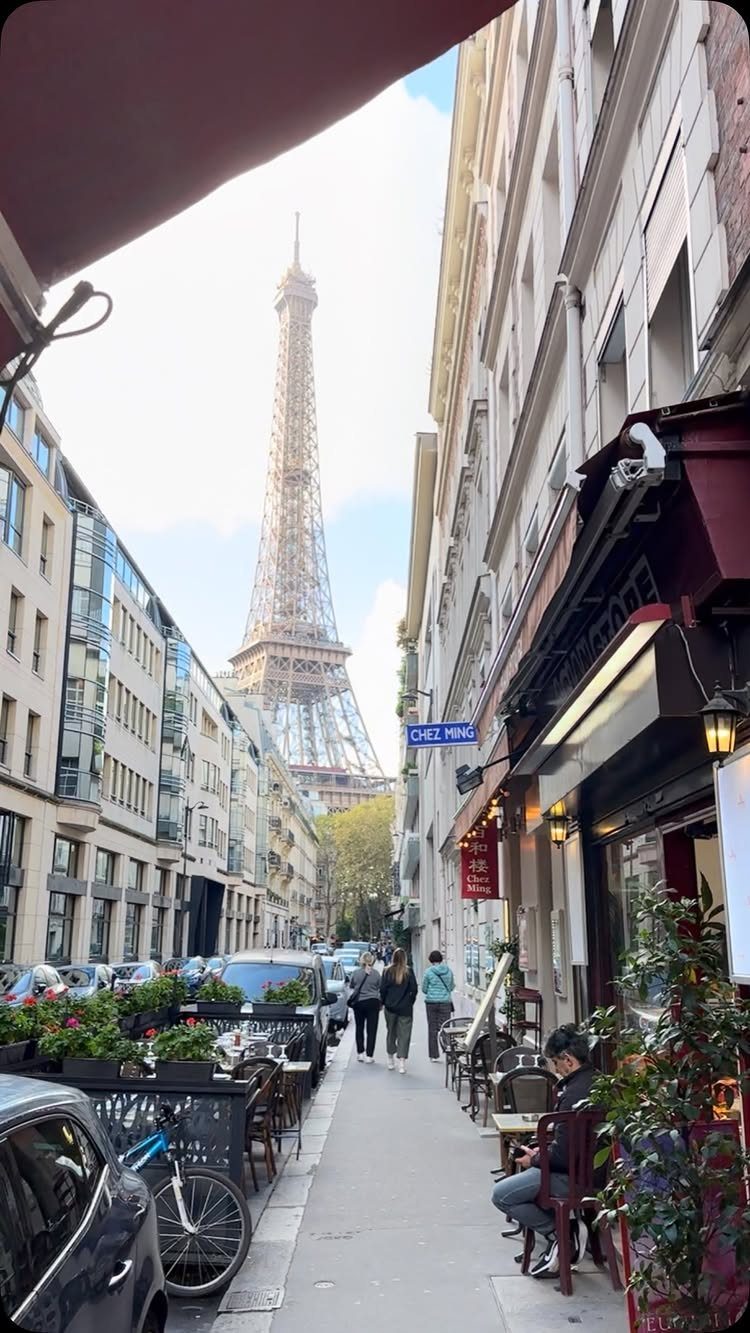 Eiffel Tower towering over a Parisian street with outdoor cafe seating and pedestrians.