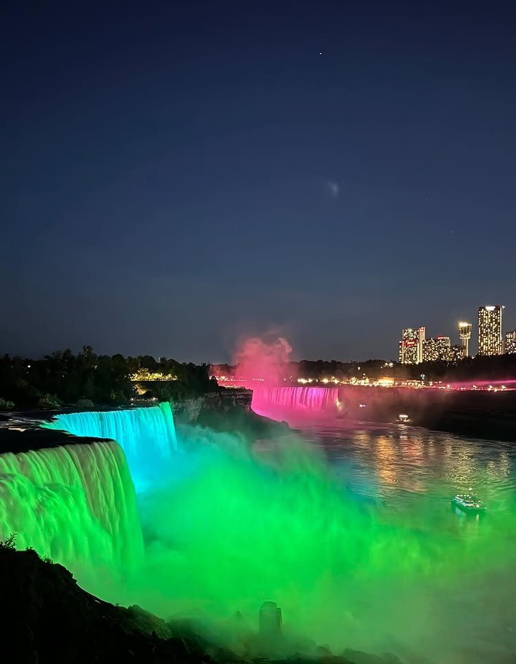 Niagara Falls illuminated with colorful lights at night with city skyline background