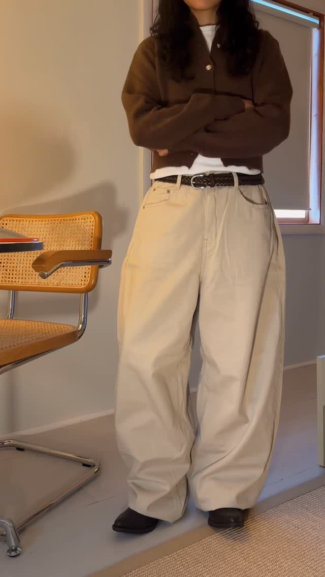 How to Pack for a 3 Week Trip: 7 Packing Ideas 2 Person wearing a brown cardigan and wide-leg beige trousers standing indoors.