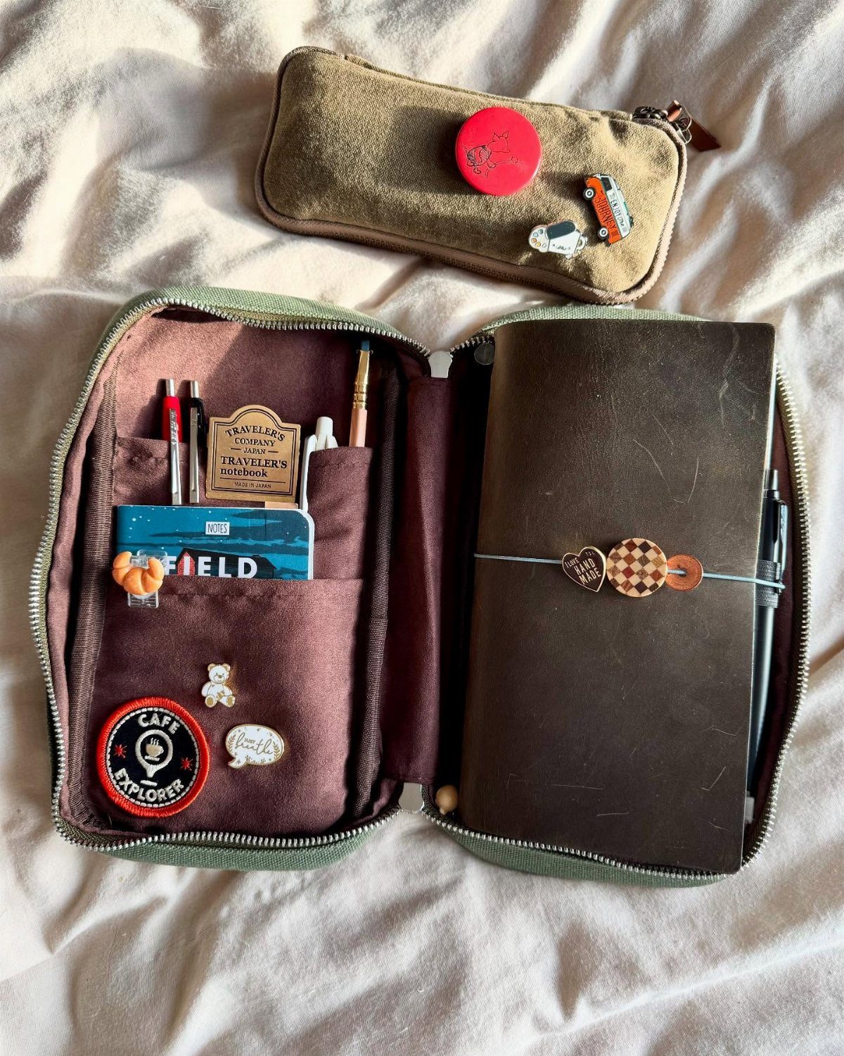 How to Pack for a 3 Week Trip: 7 Packing Ideas 4 Brown leather journal and black pen inside an open olive green travel pouch.
