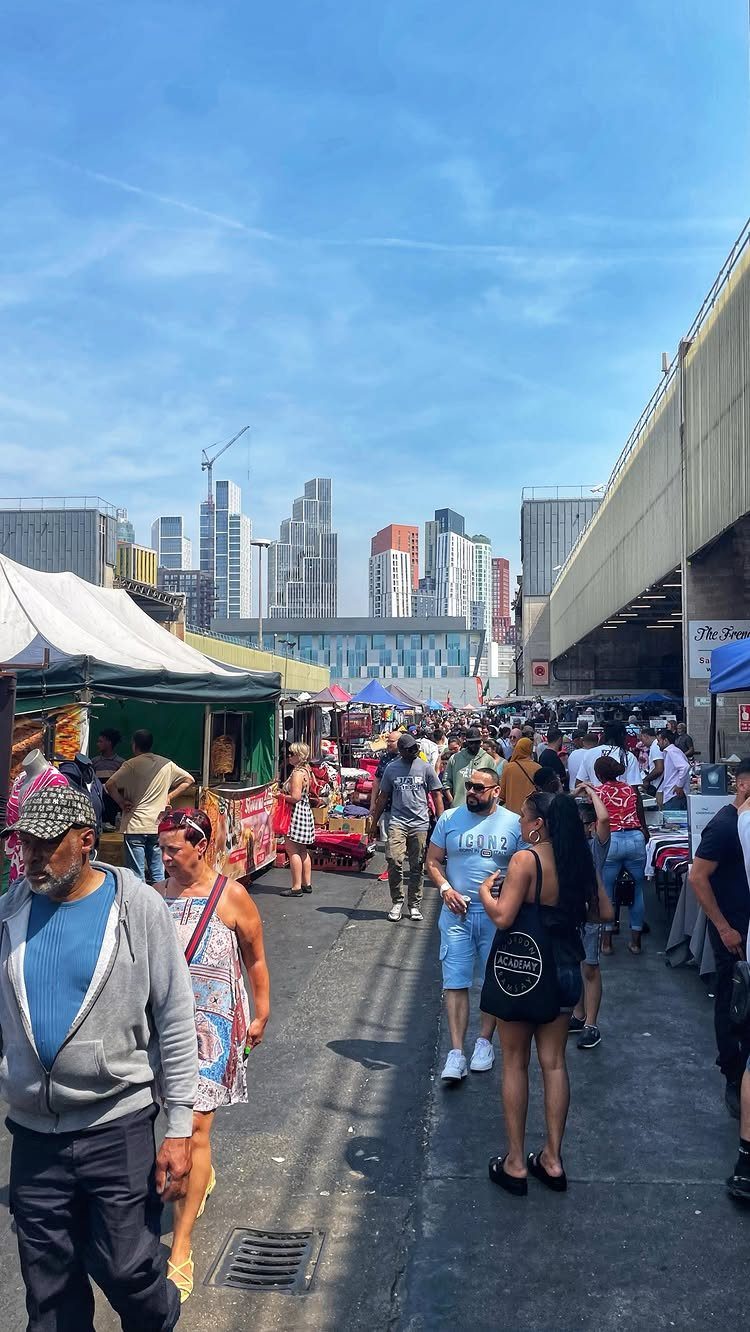 Outdoor street market with white stalls and a modern city skyline in background