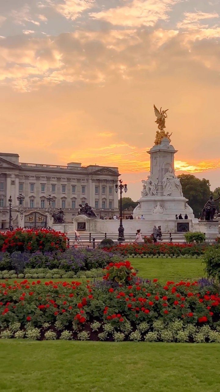 Buckingham Palace and the Victoria Memorial behind a garden of red flowers at sunset.