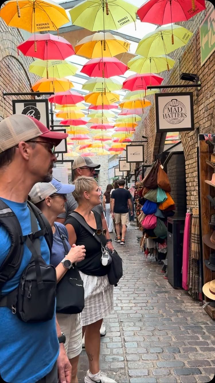 People walking under colorful suspended umbrellas in a cobblestone alley at Camden Market.