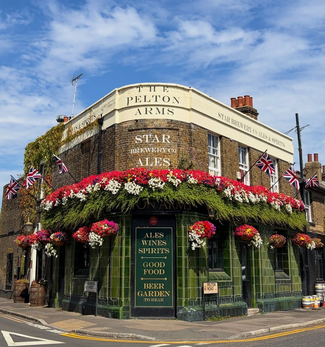 The Pelton Arms pub featuring green tiles and vibrant red and white flowers.