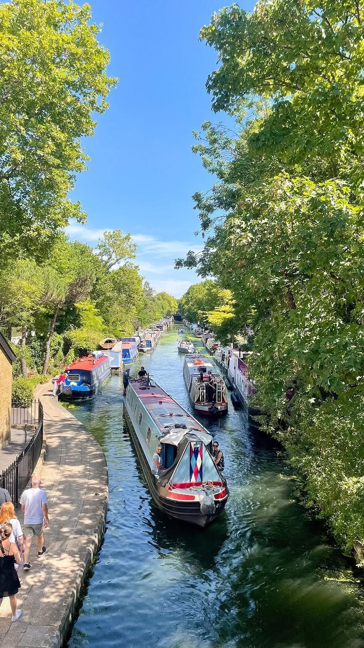 Colorful narrowboats floating on a peaceful canal surrounded by green trees and walkways.