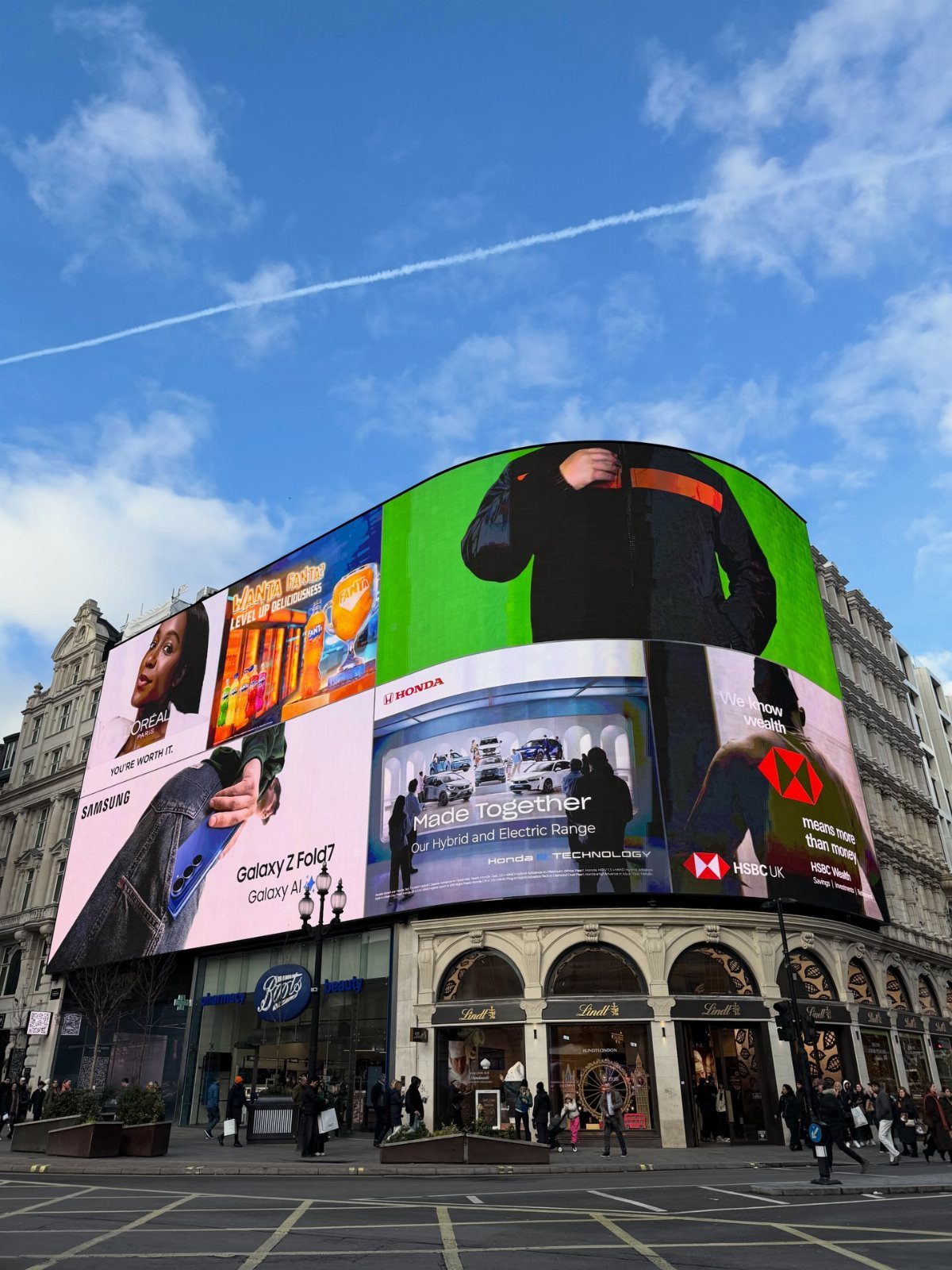Piccadilly Circus featuring a massive curved digital billboard with colorful advertisements under blue sky.