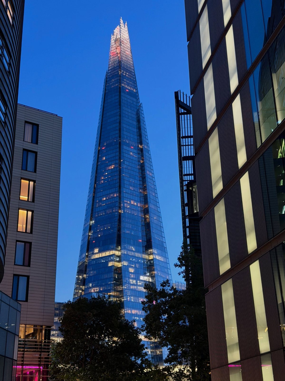 The Shard skyscraper towering over city buildings under a dark blue evening sky.