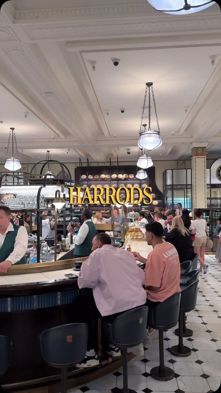 Harrods luxury food hall interior with customers at a counter and gold signage.