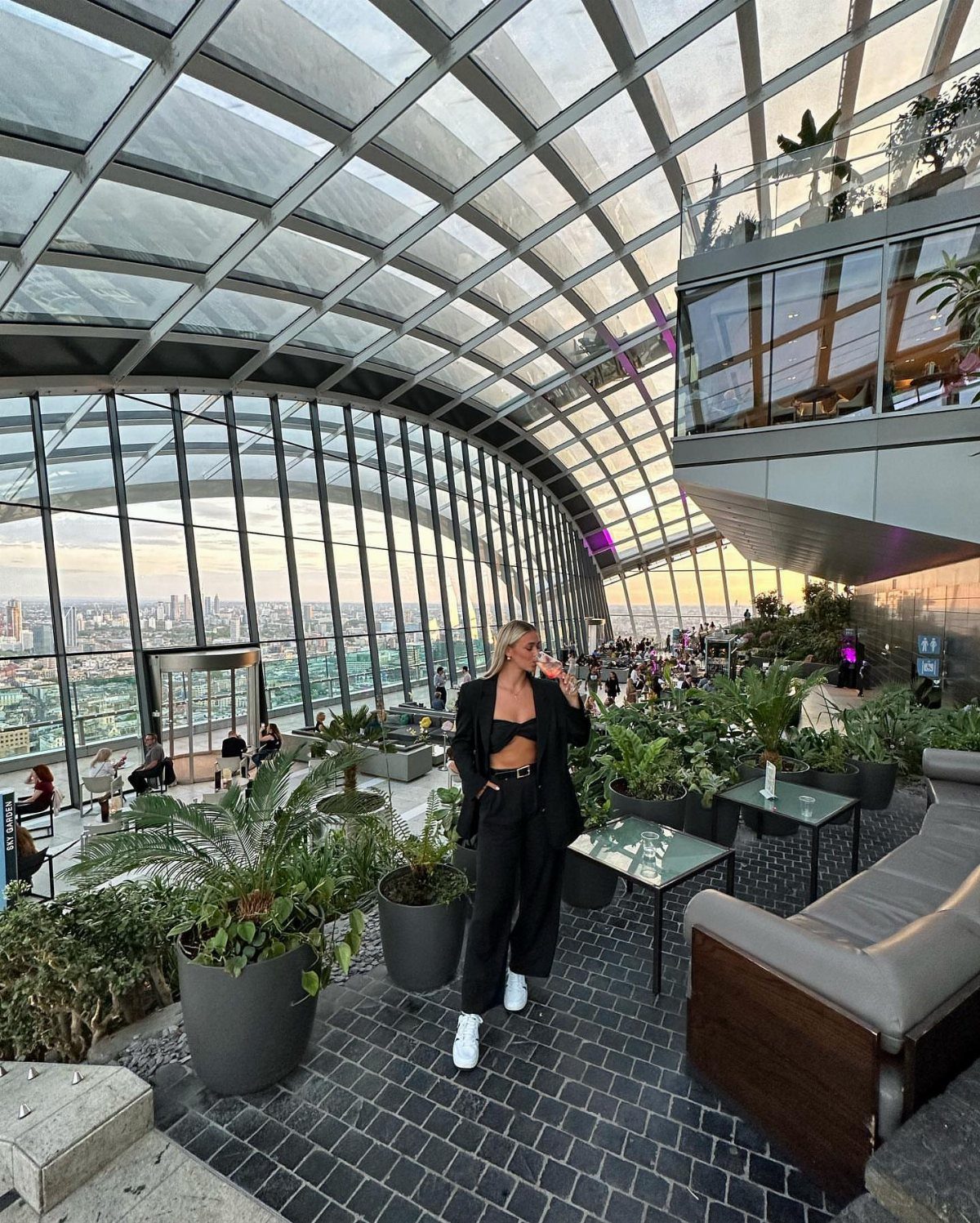 Woman standing in Sky Garden with lush plants and London city skyline views.