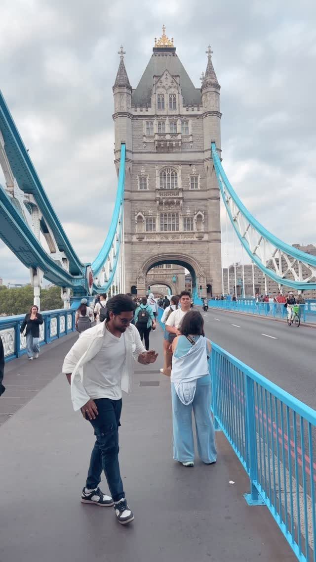 Man walking on Tower Bridge with the iconic stone tower and blue cables.
