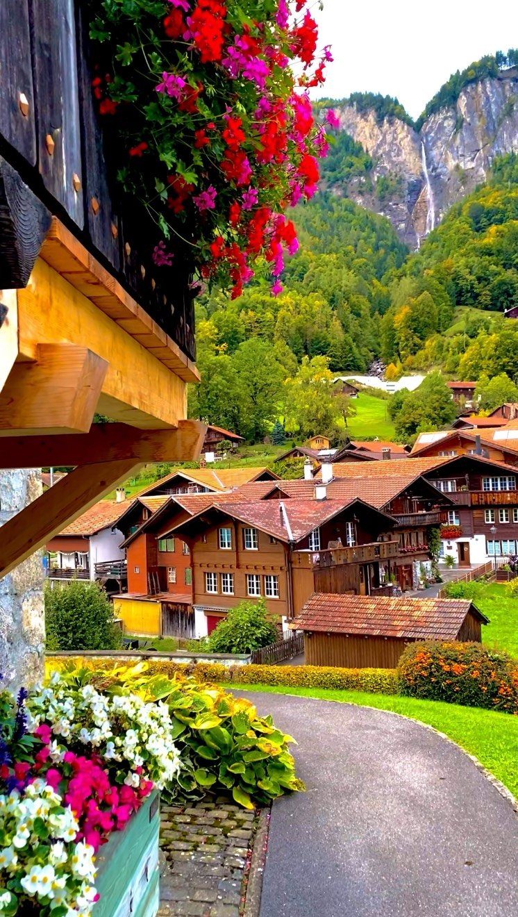 Traditional wooden chalets in a lush green valley with a distant waterfall.