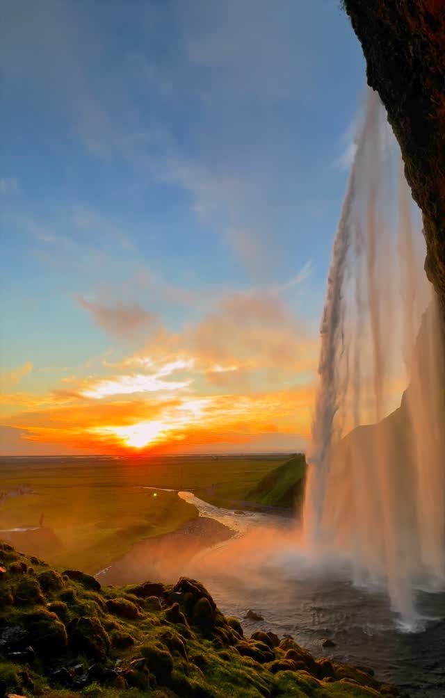 Tall waterfall cascading from a dark cliff during a vibrant orange sunset