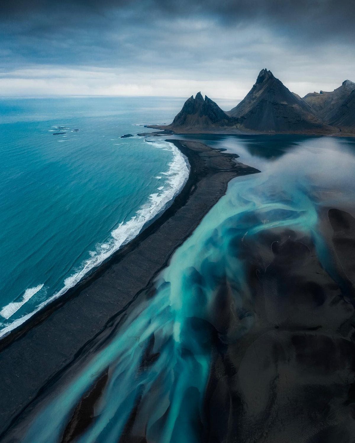 Black sand beach with turquoise glacial rivers flowing toward a blue ocean