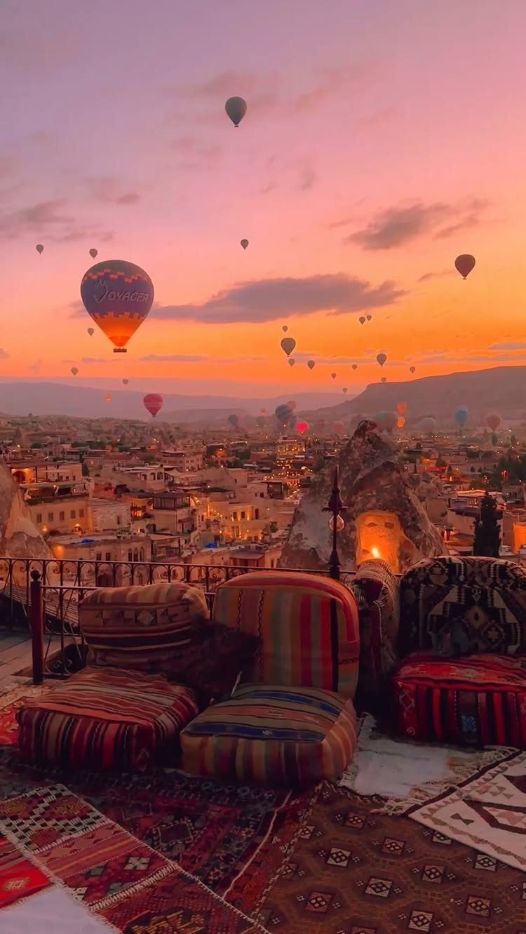 Hot air balloons floating over a stone town at sunset from a decorated terrace