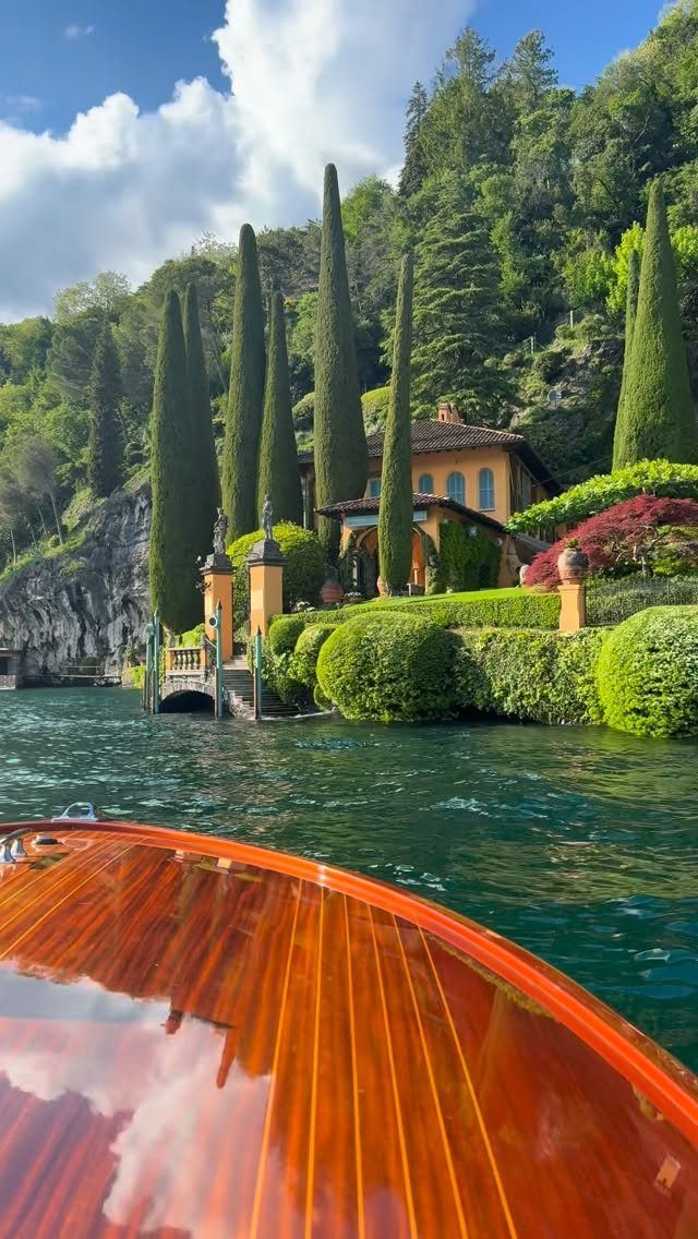 Wooden boat on turquoise water facing a yellow villa with tall cypress trees.