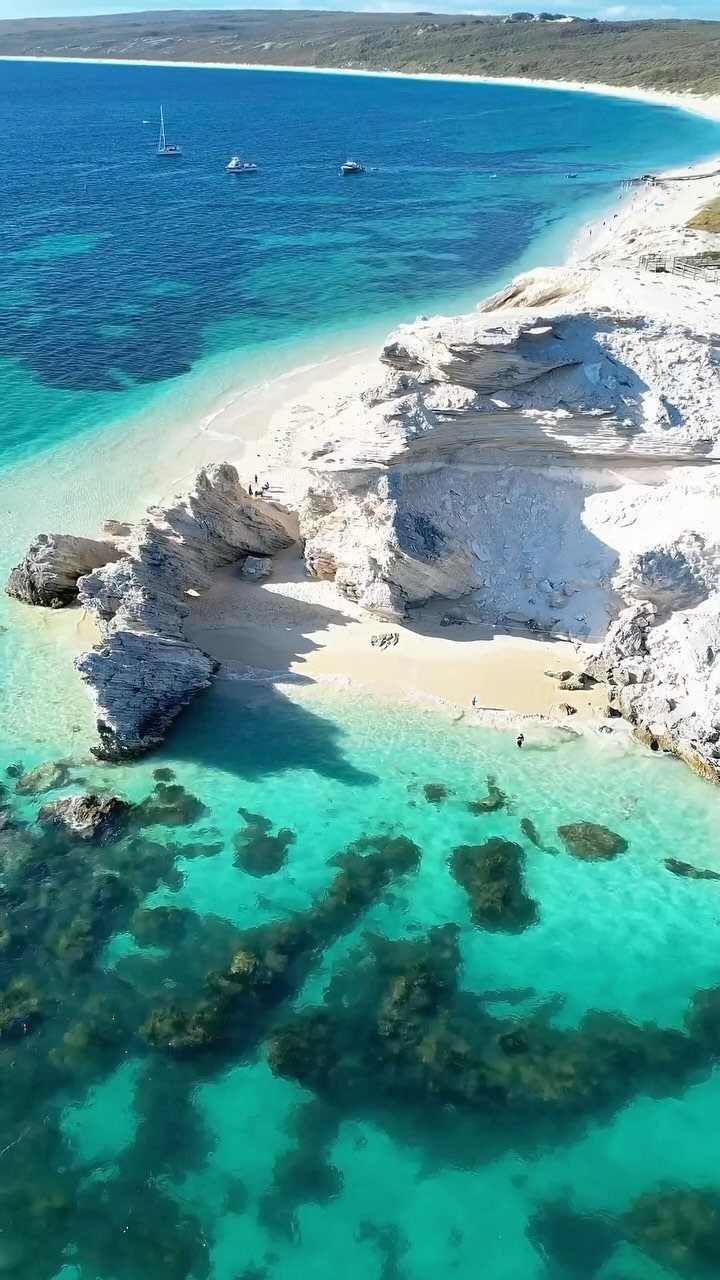 Turquoise ocean water meeting a white sandy beach and rocky limestone cliffs.