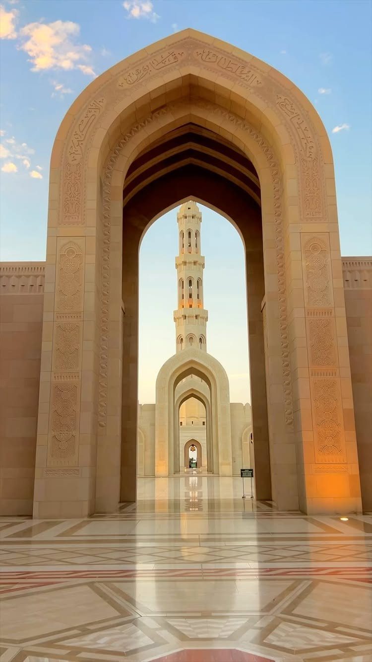 Ornate stone arches leading to a tall minaret under a clear blue sky