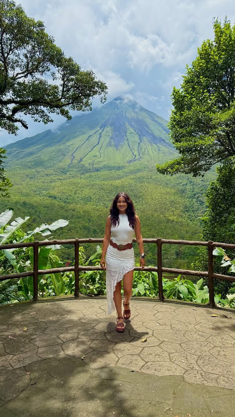 Woman in white dress posing before a large green volcano and tropical rainforest