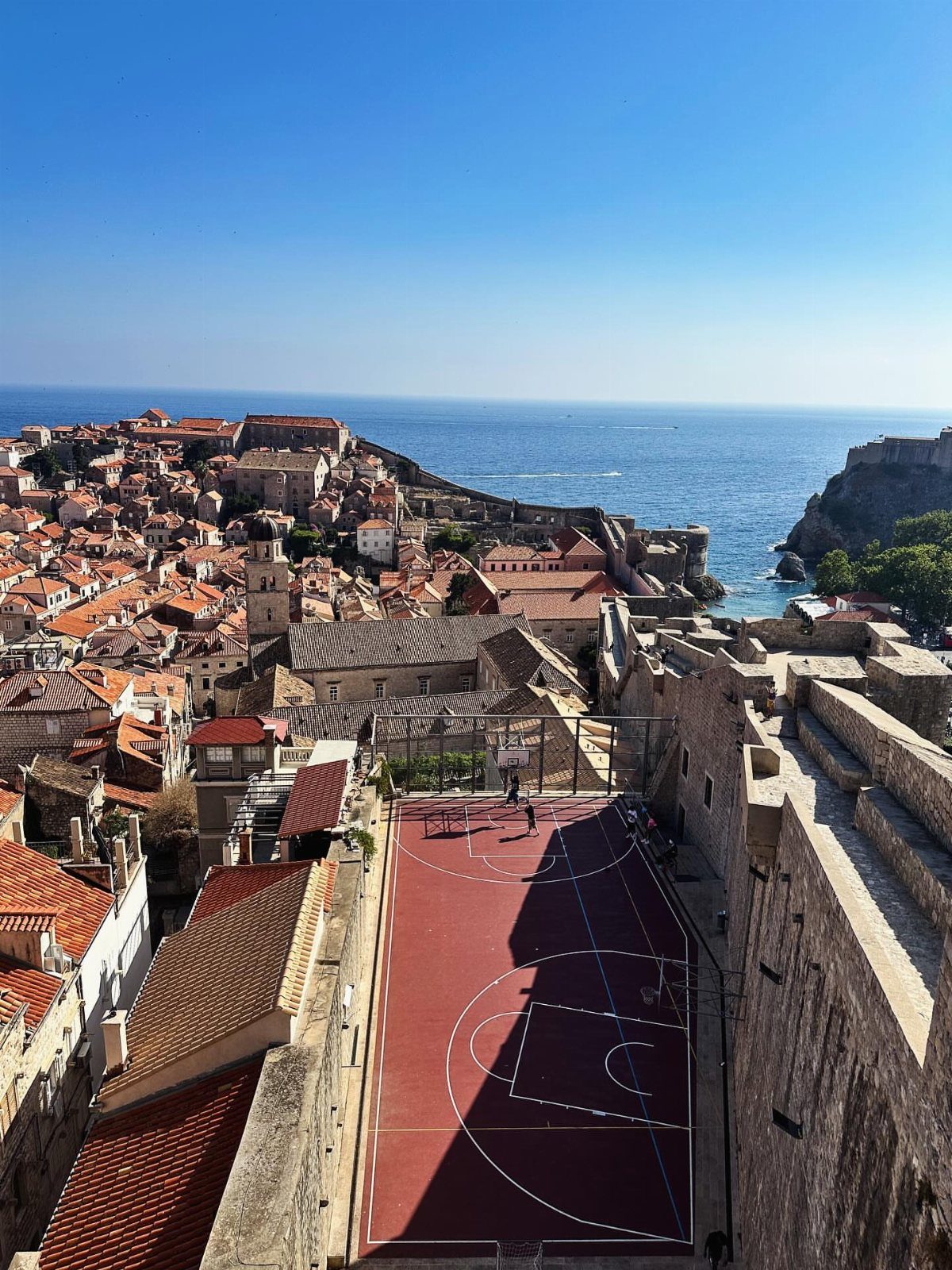 Coastal city with orange roofs and a red basketball court overlooking the blue sea