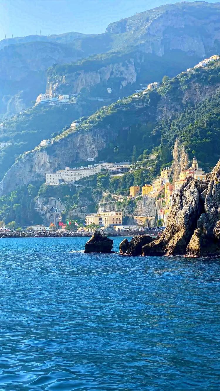 Colorful buildings perched on steep green cliffs overlooking a deep blue ocean coast.